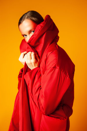 Young woman wrapping in red coat against yellow background