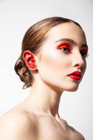 Woman with red makeup and painted ear in studioの写真素材
