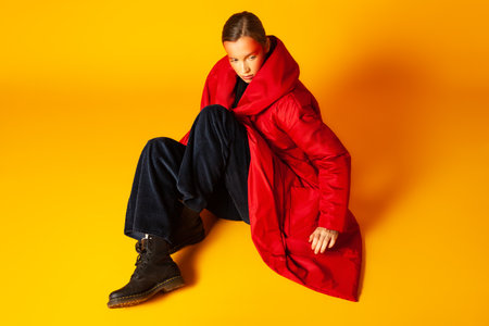 Lonely woman wrapping in baggy coat against yellow backgroundの写真素材