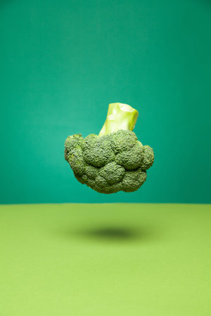 Tasty fresh broccoli head levitating in green studio