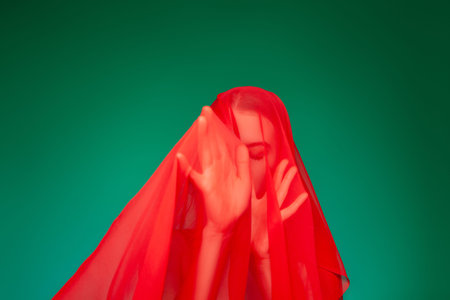 Dreamy woman under red veil against green background