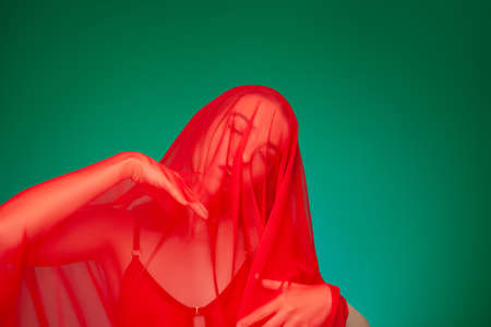 Dreamy woman under red veil against green backgroundの写真素材