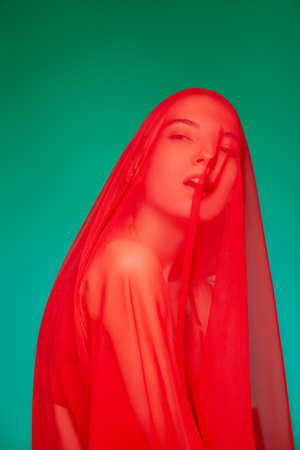 Dreamy woman under red veil against green backgroundの写真素材