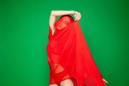 Dreamy woman under red veil against green backgroundの写真素材