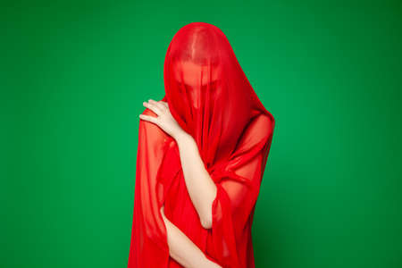 Dreamy woman under red veil against green backgroundの写真素材