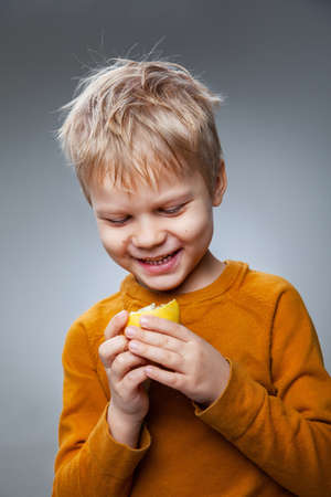 Happy child eating lemon in gray studioの写真素材
