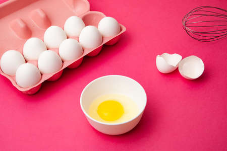 Box of eggs near bowl of yolk and whisk on pink tableの写真素材