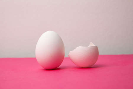 White eggs near broken shell on pink tableの写真素材