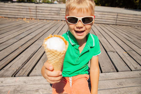 Cheerful kid in sunglasses showing ice cream coneの写真素材