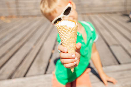 Cheerful kid in sunglasses showing ice cream coneの写真素材