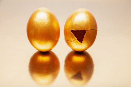 Whole and cracked Golden eggs placed on reflective tableの写真素材