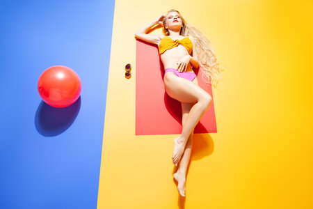 Slim woman in bikini lying on floor in studioの写真素材