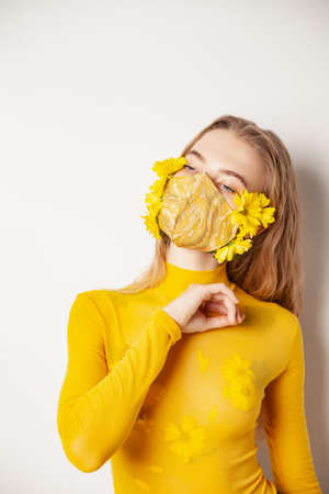 Woman in mask with yellow flowers in studioの写真素材