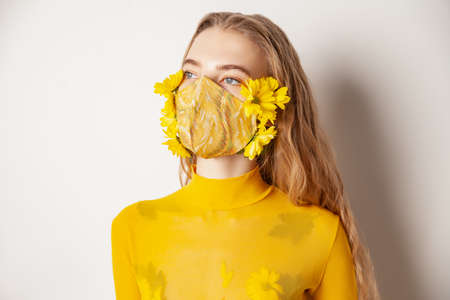 Woman in mask with yellow flowers in studioの写真素材