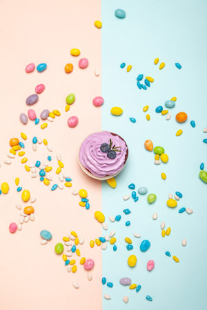 Delicious cupcake near sweet candies on peach and blue background