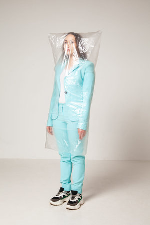 Stylish woman in plastic bag against gray background