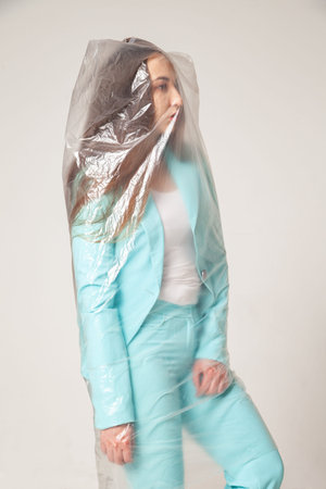 Stylish woman in plastic bag against gray background