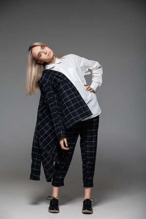 Full body young female model in trendy smart casual clothes touching head and leaning back against gray backgroundの写真素材