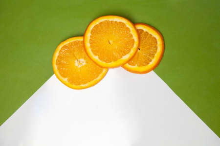 Top view of pieces of fresh natural orange placed on white and green backgroundの写真素材