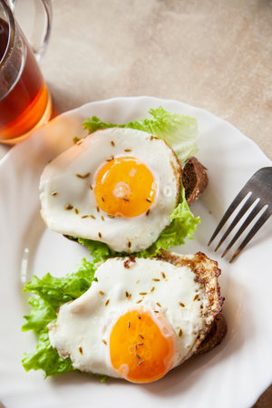 Delicious toasts with fried eggs and lettuce leaves for breakfast placed on table near cup of hot tea in morningの写真素材