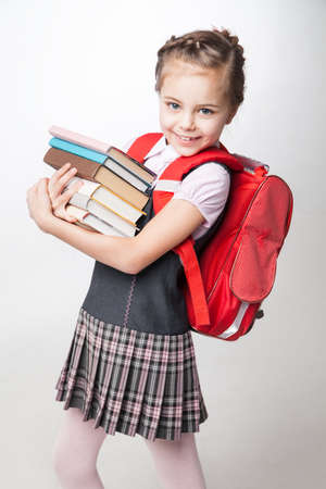 Full height portrait of a happy schoolgirl in uniform and with backpack standing on white backgroundの写真素材