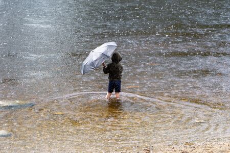 A boy holds an umbrella to shelter from the rainの写真素材