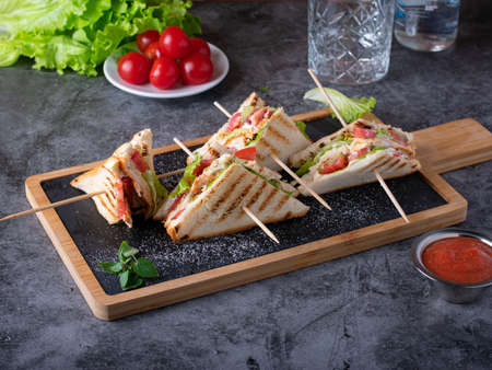 Four club sandwiches with letucce, cherry tomatoes and cheese on the boardの写真素材