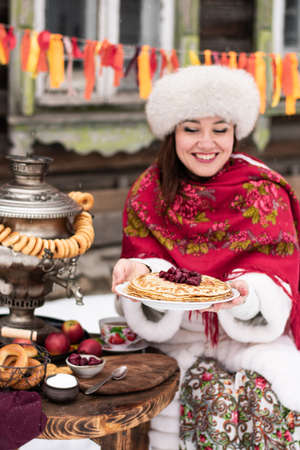 Beautiful young woman with a plate of pancakes and samovar.Shrovetide concept Maslenitsa. Verticalの写真素材