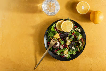 Fresh salad with orange and pomegranate seeds, baby spinach on yellow background. top view. copy spaceの写真素材