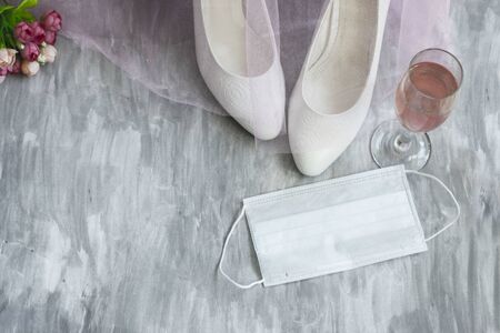 shoes on a gray background next to a medical mask and wine in a glass, pink veil and flowersの写真素材