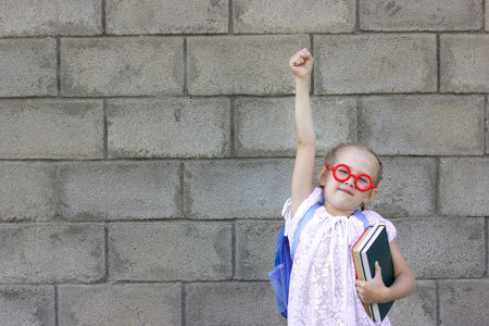 a little girl with blond hair against a gray wall to go to school, happiness is in her eyes, a...