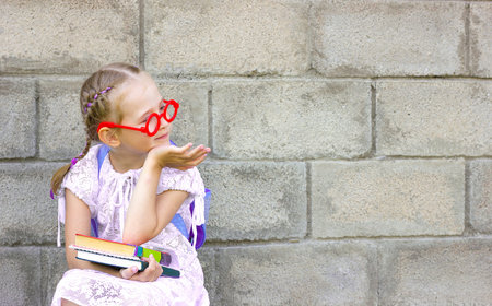 little girl with blond hair in pigtails sits on a chair with a backpack on his back and books in his...