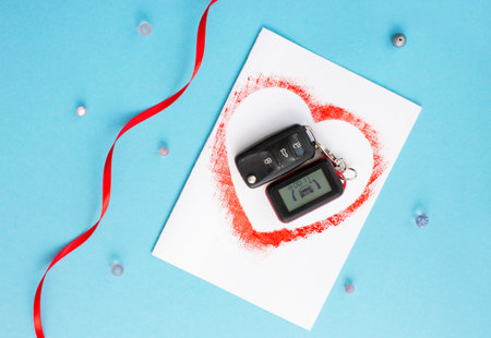 top view of car keys as a gift on homemade card with red heart on blue background with ribbons,...