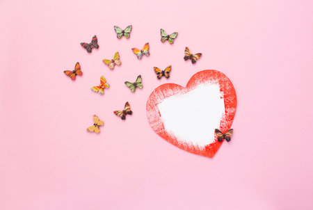 romantic composition. heart made of paper with red edges on a pink background with butterflies made of wood, valentines day conceptの写真素材