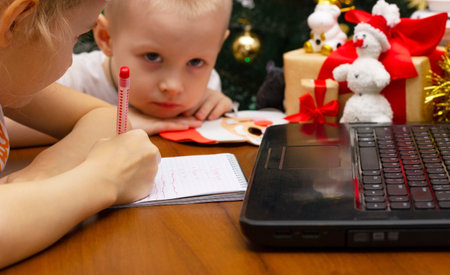 Children write a letter to Santa Claus against the background of a decorated Christmas tree, brother and sister make a wishの写真素材