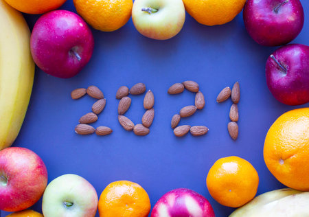 2021 from almond nuts on gray background surrounded by fruits apples, bananas, tangerines, healthy food conceptの写真素材