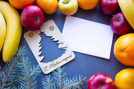 Christmas composition of fruits, white empty leaf in the middle with a wooden blank of a Christmas tree around apples, tangerines, bananasの写真素材
