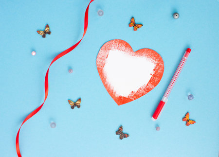 Romantic card on a blue background with a red paper heart made of paper, multicolored butterflies ribbons red pen lie aroundの写真素材