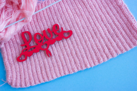 knitting needles and pink pattern of yarn on a blue background, wood lettering love, home hobby