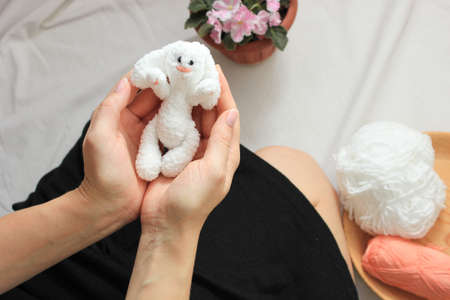 little knitted white bunny lies in the hands of a girl, the concept of a gift for a birthday, holidayの写真素材