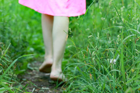 the legs of a girl are walking barefoot along a path in the forest among the green grassの写真素材