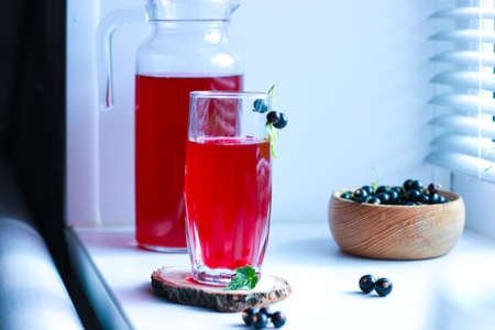 black currant juice with a glass glass on the window in the shade of the blinds, berries, summer soft drinks, healthy food.の写真素材