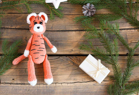DIY Christmas decor 2022, year of the tiger, crocheted orange tiger sits on a wooden background with a gift and looks at the camera with cute eyes.の写真素材