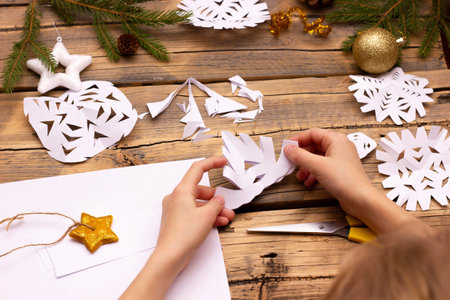 childrens hands cut snowflakes from paper at home on a wooden backgroundの写真素材