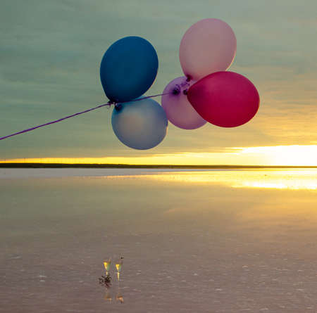 red, blue, pink, blue balloons at sunrise on a pink salt lake and glasses of champagneの写真素材