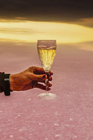 glass of champagne in hand against at sunrise on the pink lake Lemurian Ukraineの写真素材