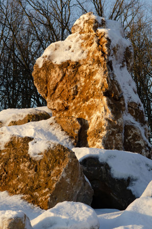 Winter landscape with rocks laid out in a bizarre pattern covered with snow against a backdrop of a leafless forest on a sunny day.の写真素材