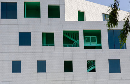 Modern white building facade with geometric windows and green interior staircase under bright daylight urban architectureの写真素材