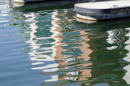 Boats and floating docks reflected in calm marina water under bright sunlight and peaceful coastal ambianceの写真素材