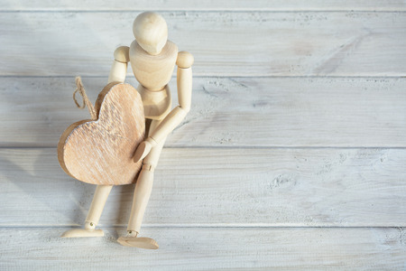 The dummy sits on the board and holding a wooden heart.の写真素材